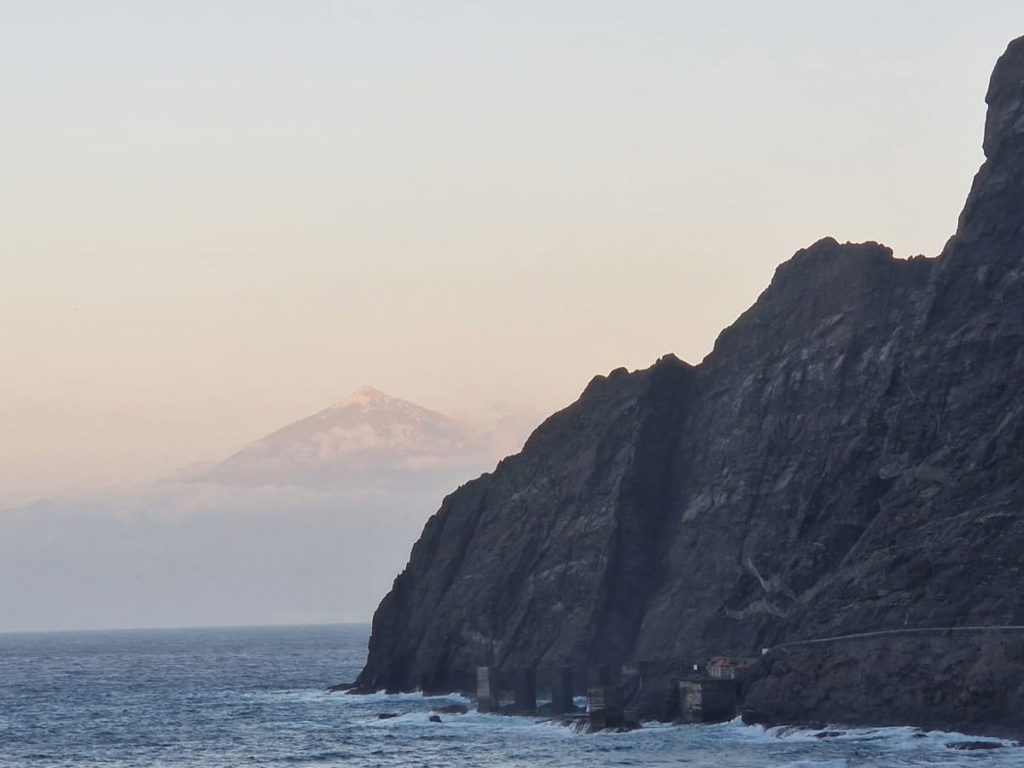 Ruine einer alten Verladestation vor Felsen im Meer, dahinter der Teide